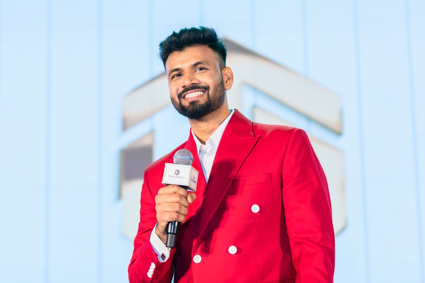 Purushottam smiling on stage with a mic at a live event