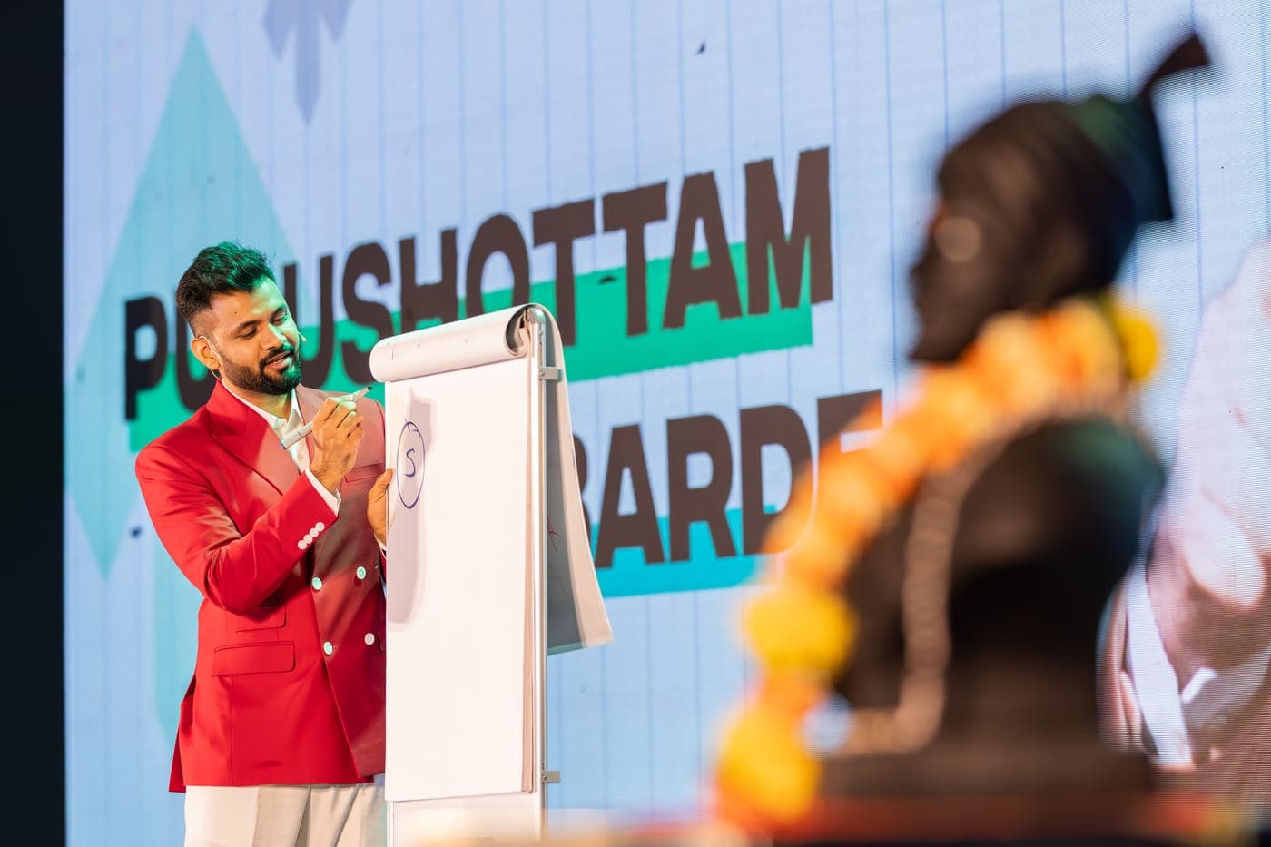 Purushottam teaching on stage with a garlanded bust of Chhatrapati Shivaji Maharaj in the foreground